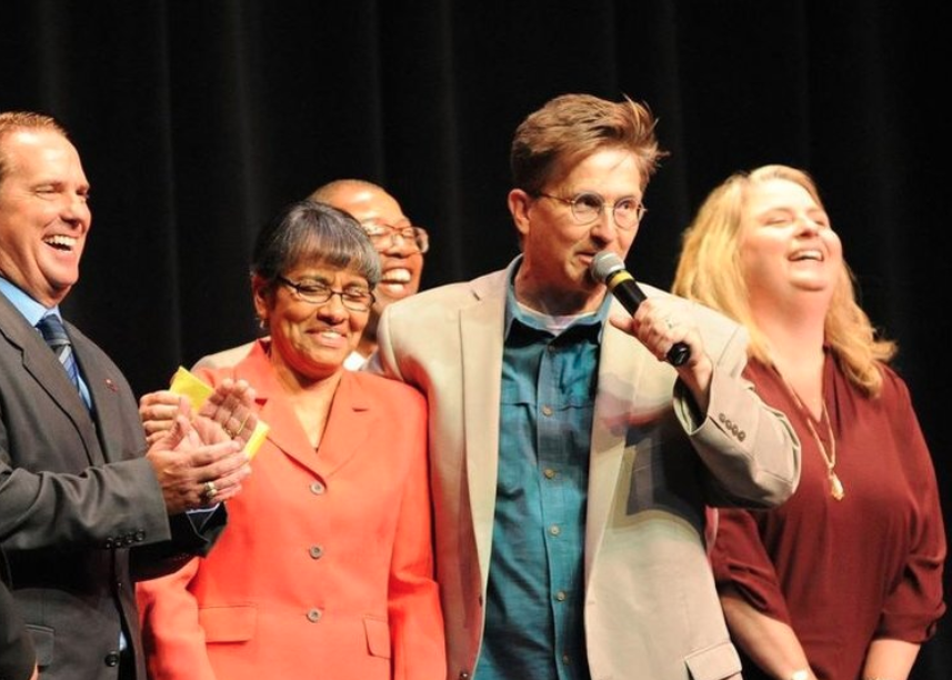Tim Clue laughing on stage arm in arm with participants